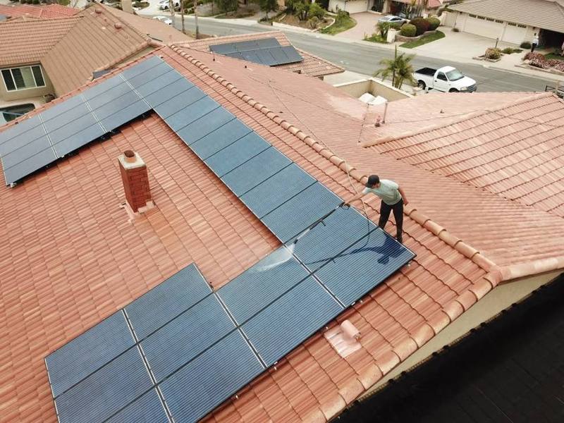 Technician cleaning solar panels on a tile roof